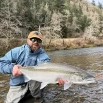 Founder Devyn Christian holding a large steelhead on a forest river